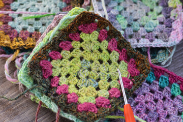 Closeup of craft work of crochet granny squares in mute rainbow colours with a crochet hook. Beautiful ball of hand spun yarn on a traditional spinning wheel.