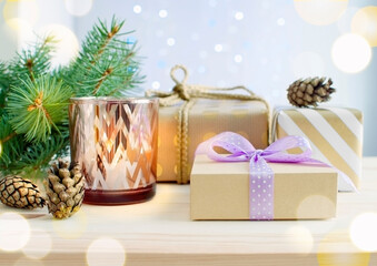 Christmas gift boxes against a bokeh background, with a candle, fir cones, and fir branches