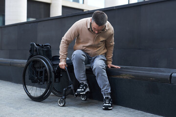 Young man with disability trying to sit in wheelchair while spending time outddoors