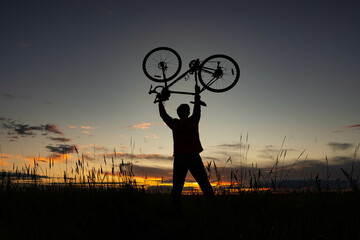 cyclist silhoutte with bicycle raised to sky race and victory concept on the background of a beautiful sunset