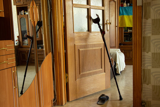 An Elbow Crutch Stands Near The Door In The Apartment And On The Background Of The Flag Of Ukraine, Rehabilitation After An Injury In The War In Ukraine At Home