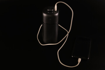 Obraz premium powerbank black on a black background, usb cable, smartphone, plug, light and reflection