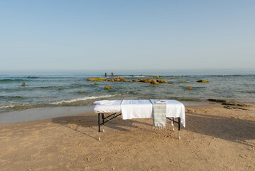 Fototapeta na wymiar Massage table on the beach near the sea prepared by professional masseur for relax in tropical massage spa procedures.