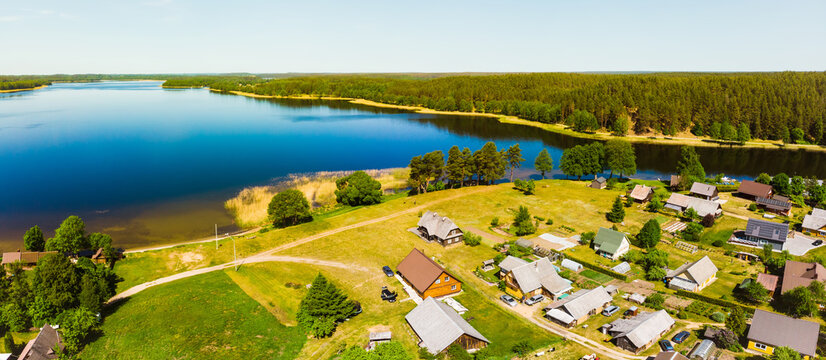 Lusiai lake panorama aerial view with cars on road drive pass vintage houses in Paluse village - famous travel destination in Lithuania, Baltics, Europe