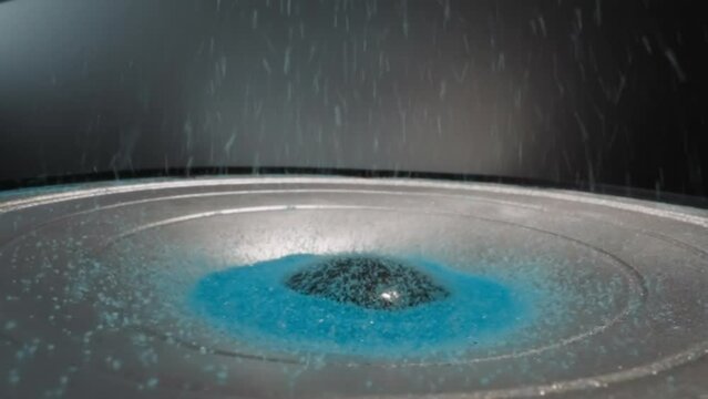 Loudspeaker plays music and throws blue hydrophobic sand upward. Colored aquarium sand moves depending on intensity of sound waves. Demonstration of acoustic system operation macro