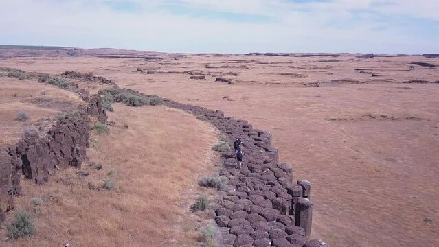 Aerial follows two photographers on top of basalt column cliff in WA