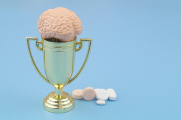 Human brain with winner trophy cup and medical pills on blue. Copy space for text.