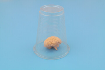 Trapped human brain under plastic cup on blue background.