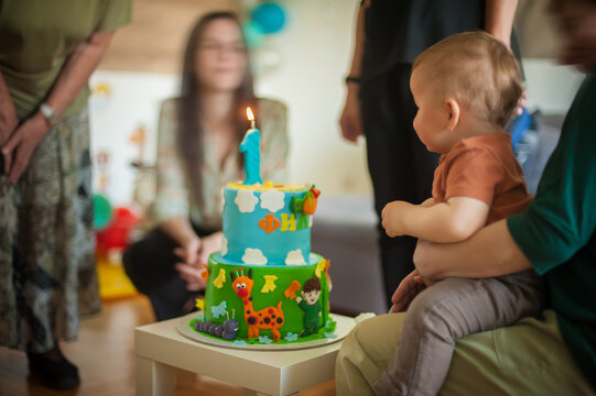 Cute baby boy celebrates his first birthday with his family at home. Cake and candle in the shape of number one