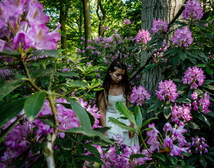 A girl in a white dress stands among the purple flowers in the forest
