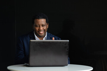 Portrait of handsome black man wearing suit and using laptop computer while sitting