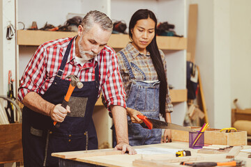 Senior professional caucasian male diy wood working making fix home furniture in workshop wife helping.