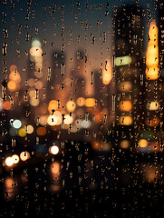 Close up photo of rain drops on the window, behind which is a blurred night cityscape with traffic lights