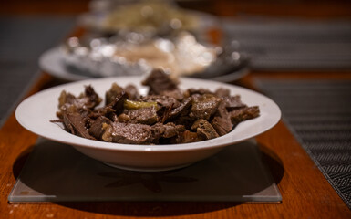 Slow cooked beef stew on a plate together with out-of-focus dishes on a wooden table. Home cooking and entertainment concept.