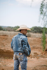 Cowboy wearing jeans and a hat, standing under the sky with fluffy clouds, working on a farm
