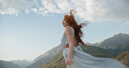 Gorgeous caucasian girl wearing a light dress is posing for a photo shoot on scenic mountain...