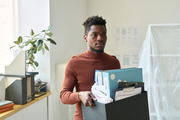 African American businessman carrying box with office stuffs during the move in new office