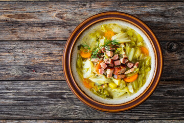 Bowl of hot cabbage soup with bacon on wooden table
