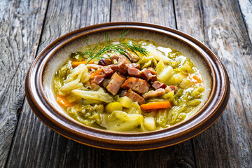 Bowl of hot cabbage soup with bacon on wooden table
