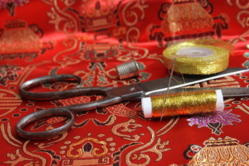 Spool of Gold Metallic Thread and Thimble on Vintage Red Silk Fabric