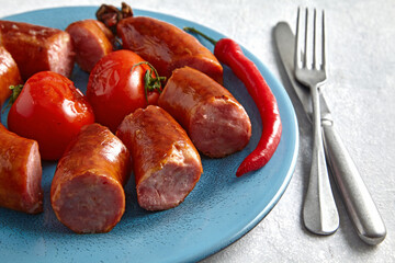 Fried pork sausage cut into pieces in a blue plate with tomatoes and cutlery