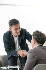 Smiling asian businessman shaking client hand, closing successful deal, satisfied hr manager hiring new employee, business partners handshaking at meeting.