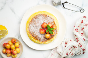 Japanese cotton cheesecake with cherries and powder sugar on top. White marble background