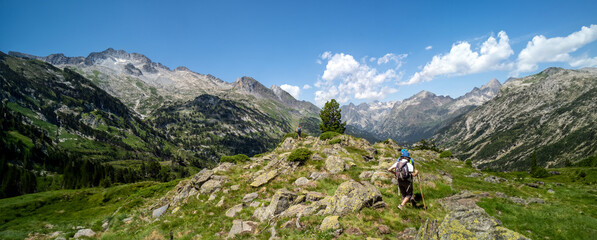 Woman hiker on top of a mountain and two people approaching watching and contemplating the mountainous landscape of the high peaks of the green and leafy Pyrenees.