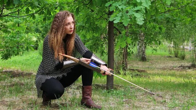 Smooth camera movement, selective focus, a young woman in chain mail and bracers with a bow in her hands sits against the backdrop of a summer forest.