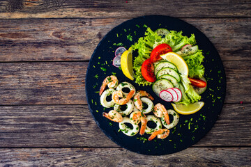 Fried prawns and calamari rings with fresh vegetables on wooden table
