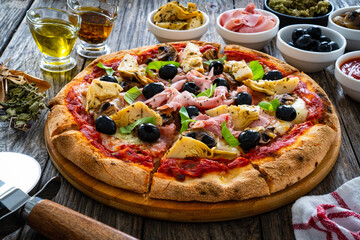 Pizza capricciosa with cooked ham, mozzarella, artichoke and vegetables on wooden table 