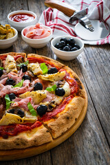 Pizza capricciosa with cooked ham, mozzarella, artichoke and vegetables on wooden table 