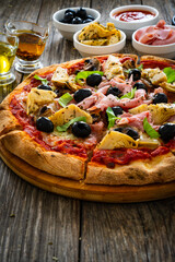 Pizza capricciosa with cooked ham, mozzarella, artichoke and vegetables on wooden table 