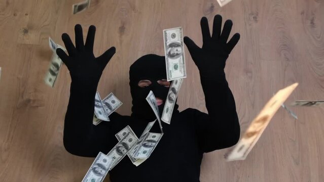 A robber in a black mask tosses dollars. A successful bank robbery