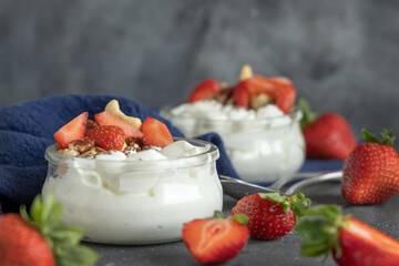 Glass jars of yogurt, nuts and strawberries on grey table with a spoon close up, copy space