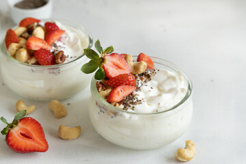 Glass jars of yogurt, nuts and strawberries on a white table close up, copy space