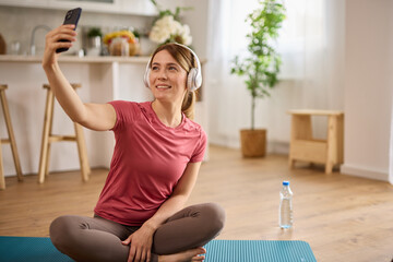 Young woman using cellphone and taking Selfie while exercising yoga at home