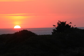 at the sea the red-golden sun shines out from behind the clouds before it sets