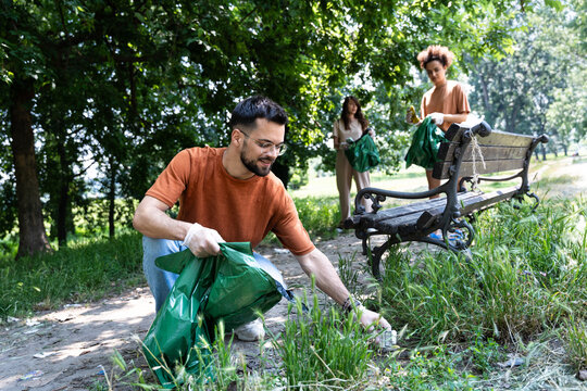Young volunteers cleaning up park together, collecting trash and holding garbage bags. Responsible parents and friends cleaning public park from litter before children come to play outside in nature.