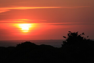 at the sea the red-golden sun shines out from behind the clouds before it sets
