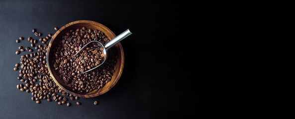 Coffee beans with metal scoop on dark background, top view. Stillife with heap of roasted Arabica grains in wooden bowl, decor for coffee shop.