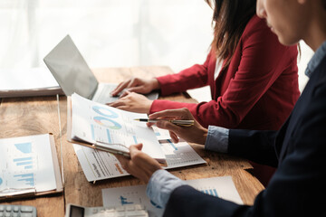Team of two asian male and female business people working together discussing new financial graph data on office table with laptop and digital tablet.