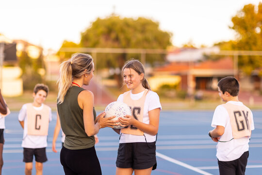netball coach interacting with girl holding ball at netball training