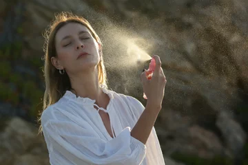 Fototapeten Woman spraying facial mist on her face, summertime skincare concept © triocean