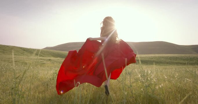 Young happy fantasy ginger woman queen runs walks in green nature whirls dances fluttering skirt red dress waving in motion. Vintage summer clothes. Candid woman princess bride. Back rear view