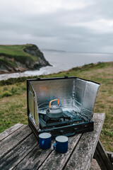 A serene camping adventure unfolds on a cliff's edge, where a gas oven sits atop a table, ready to fuel culinary delights amidst breathtaking scenery.