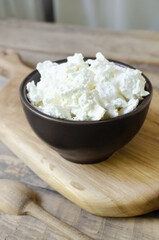 Organic cottage cheese in a brown ceramic bowl on a wooden cutting board. The concept of homemade food. Selective focus. Vertical orientation.
