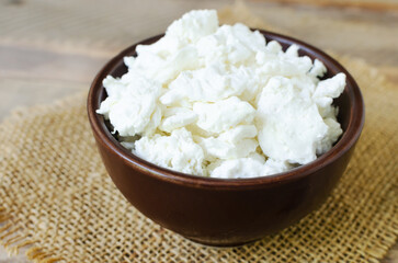 Organic cottage cheese in a brown ceramic bowl on burlap on a wooden background. The concept of homemade food. Top view. Horizontal orientation.