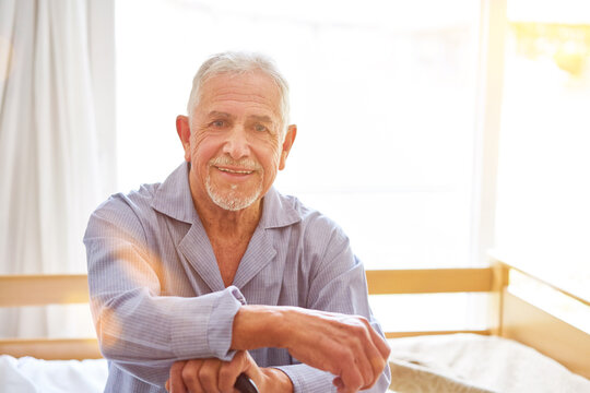 Happy Senior Man Sitting In Nightwear On Bed In Nursing Home