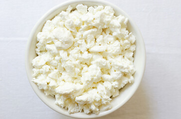 Organic cottage cheese in a white ceramic bowl on a white tablecloth. Healthy breakfast. Concept of healthy food. Selective focus. Horizontal orientation. Top view. Cpy space.